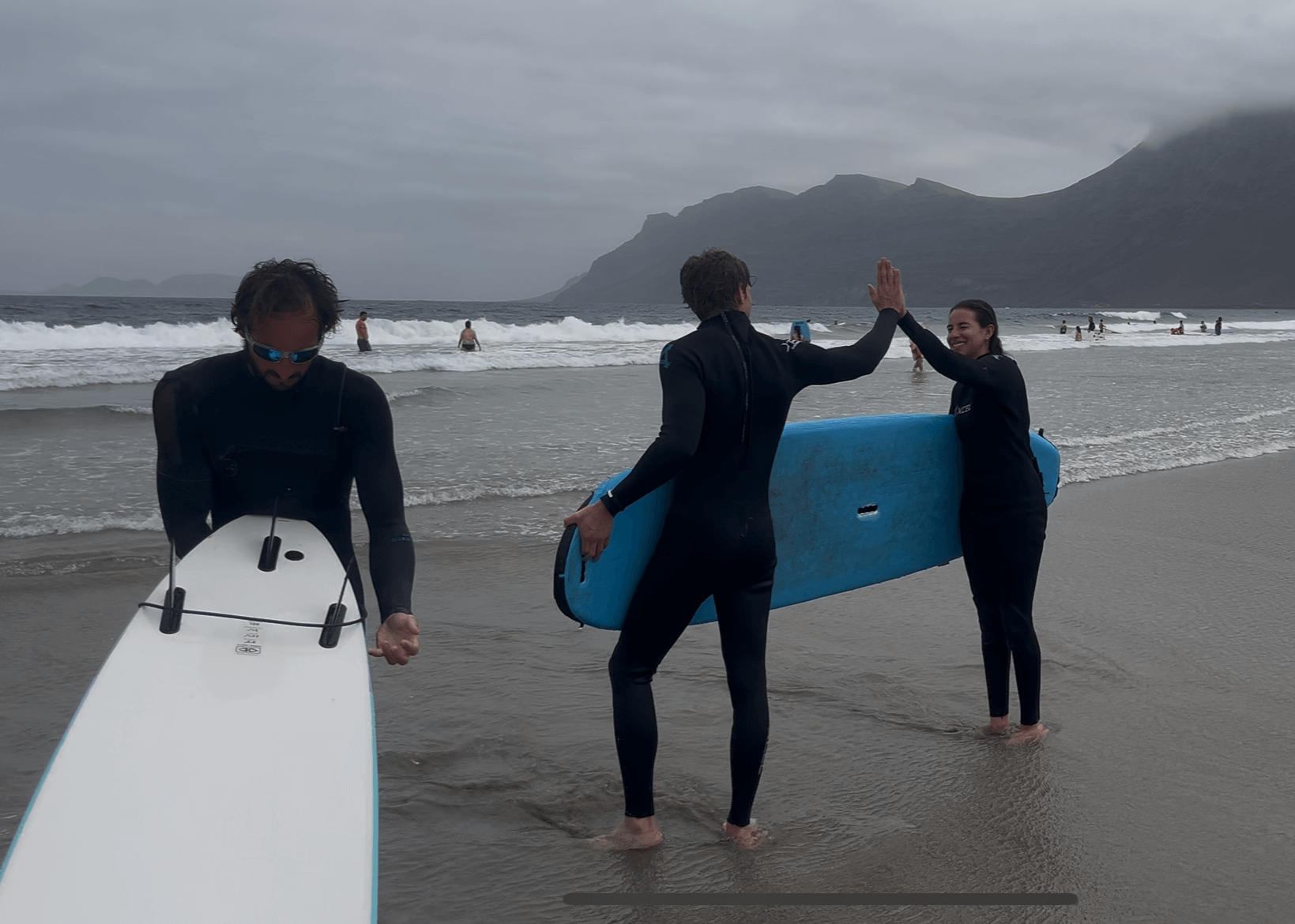 Two people in wetsuits with surfboards high-fiving on Famara Beach during a private surf lesson in Lanzarote