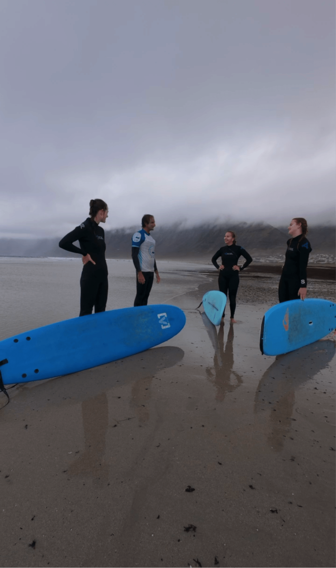 Group of surfers preparing for a private surf lesson on a cloudy beach in Lanzarote with surfboards on the sand