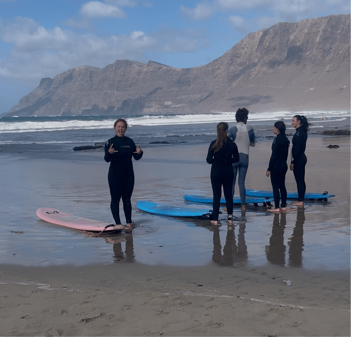 Group taking 1-day surf course on Famara Beach with surfboards and instructor in wetsuits