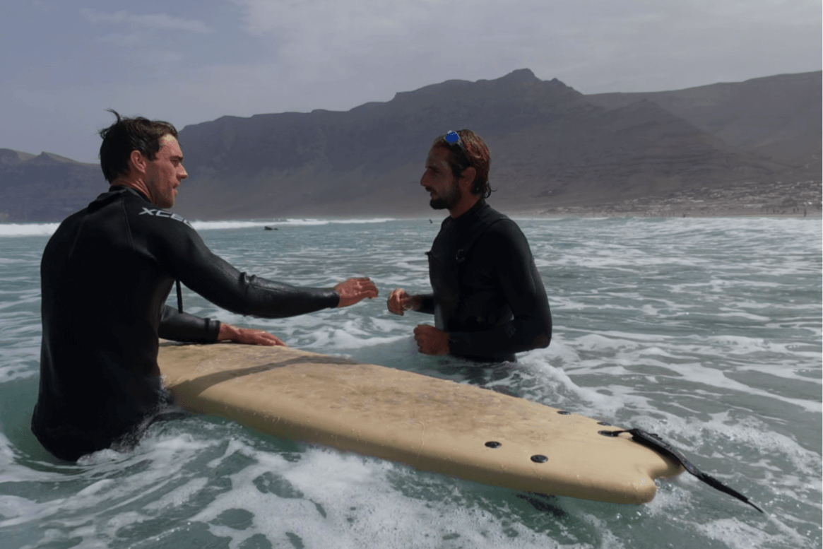 Two surfers in wetsuits discussing on a surfboard in the ocean during a private surf lesson at Famara Beach, Lanzarote.