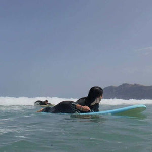 Private surf lesson for two people on Famara Beach in Lanzarote with a blue surfboard and ocean waves