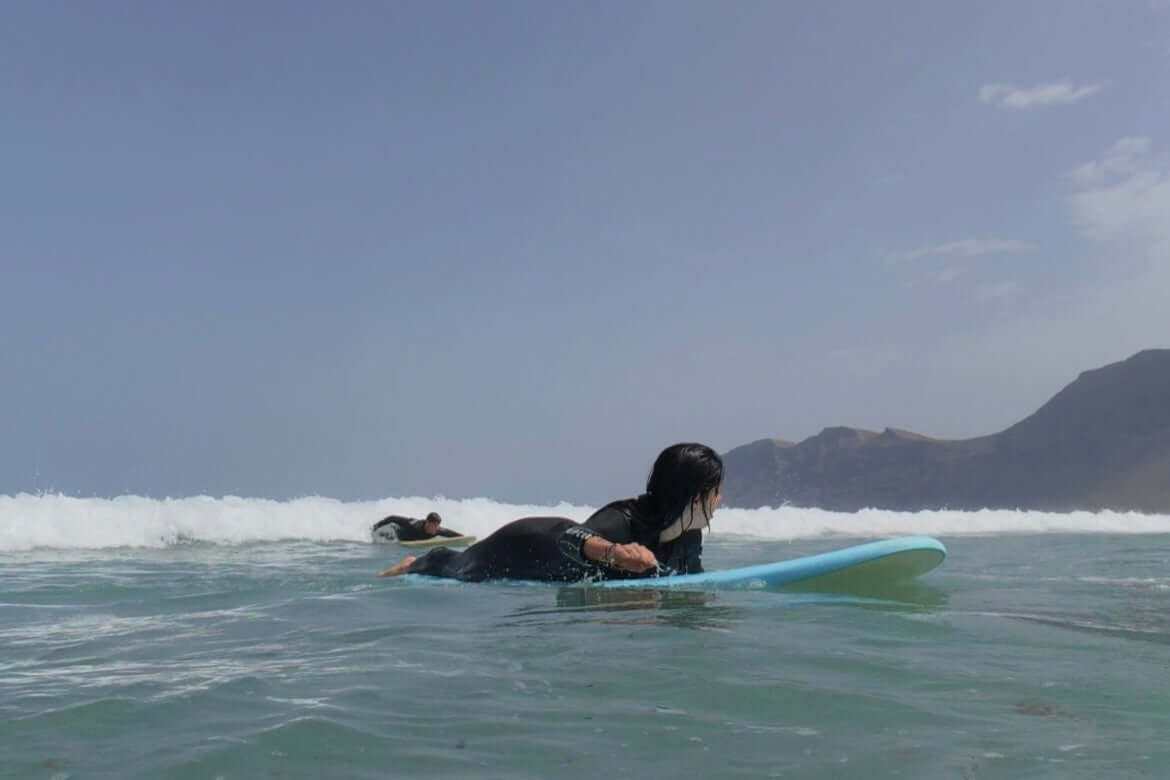 Private surf lesson for two people on Famara Beach in Lanzarote with a blue surfboard and ocean waves