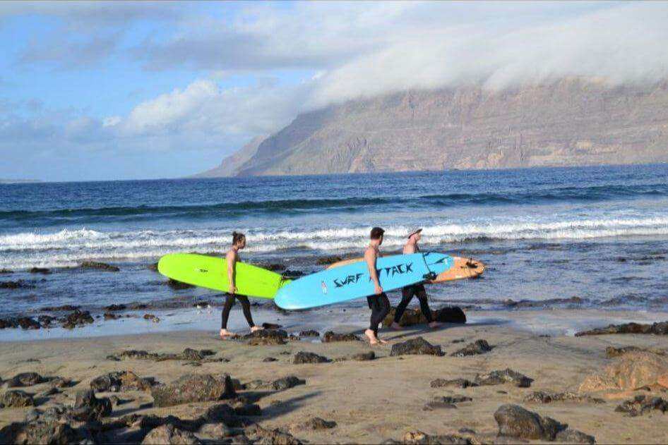 Group carrying surfboards on Famara Beach for 1-day surf course at Surf Attack in Lanzarote