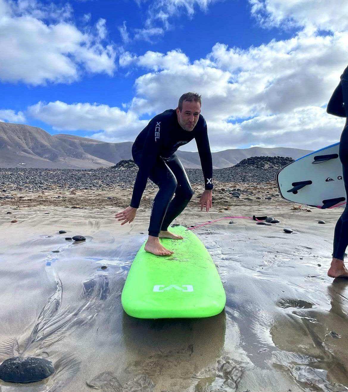 Man practicing surfing stance on a green surfboard during a private surf lesson on a beach in Lanzarote