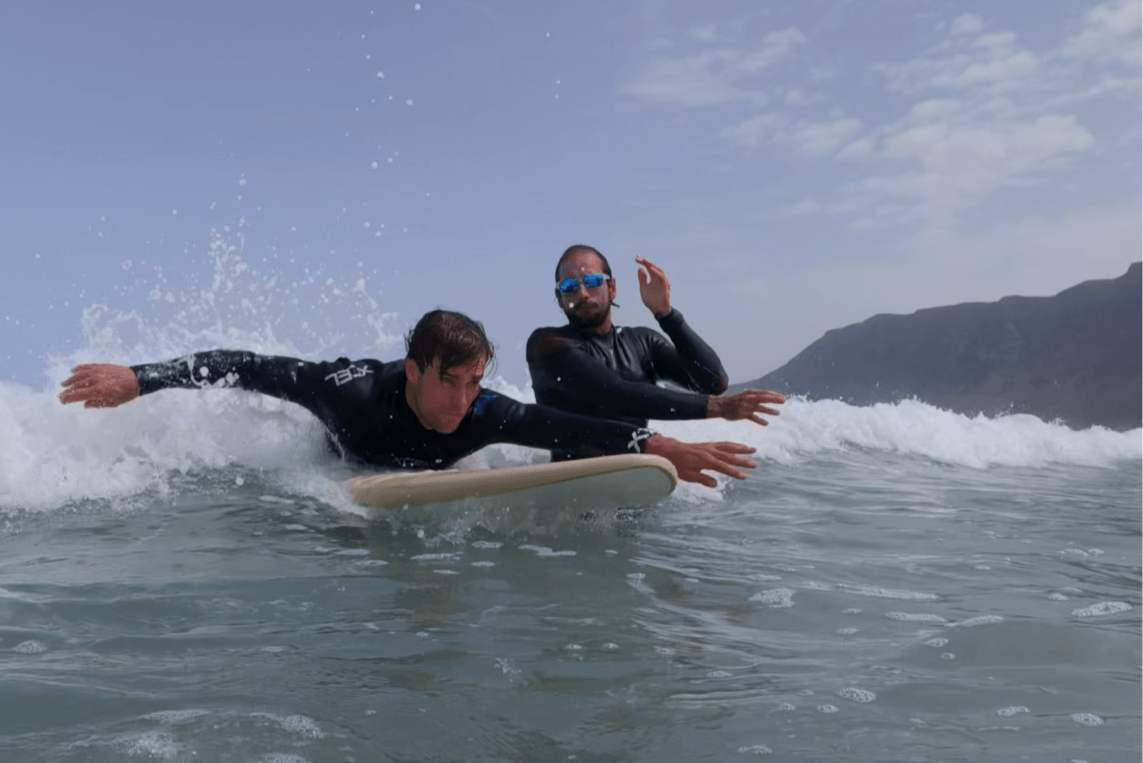 Private surf lesson with instructor coaching a beginner riding a wave at Famara Beach in Lanzarote